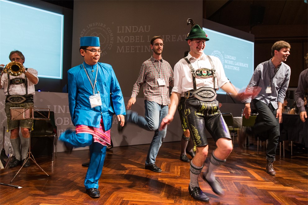 Young scientists in traditional clothes dancing with Bavarian dancers at the Bavarian Evening of the 5th Meeting on Economic Sciences.